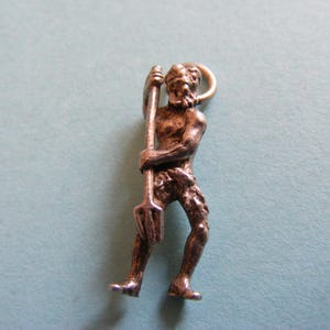 May include: A silver-toned metal charm depicting a standing figure with a beard, holding a long-handled three-pronged pitchfork in both hands. The figure has a textured surface and includes a small circular jump ring at the top for attachment.