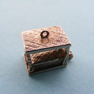 May include: A miniature silver well charm with a textured roof and detailed sides. The interior of the well is visible. A small loop is at the top for attachment. The charm is set against a light blue background. The well charm is likely a pendant.