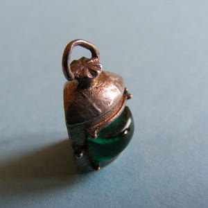 May include: A vintage silver-toned pendant with a teardrop-shaped, emerald-green glass stone. The pendant has a decorative bail and a detailed, textured metalwork design. The gemstone is smooth and polished.