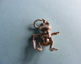 May include: A gold-colored frog charm with an umbrella. The frog is wearing a suit and has a loop at the top for attaching to a necklace or bracelet. The charm is detailed and three-dimensional.