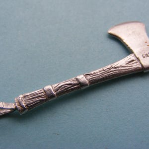 Op de afbeelding: Zilverkleurige bijl hanger met een getextureerde handgreep en het woord "SILVER" gestempeld op het blad. De bijlkop is licht zilverkleurig en de handgreep heeft een houtnerf textuur.