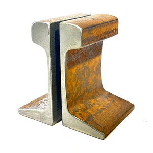 May include: A pair of bookends made from repurposed railroad track. One bookend is silver and the other is rusty brown.