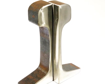 May include: A pair of bookends made from polished metal, one with a rustic finish and the other with a shiny finish. The bookends are shaped like railroad tracks.
