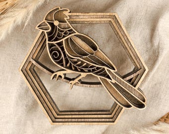 May include: A layered wooden bird sculpture, featuring a detailed cardinal design. The bird is perched within a hexagonal frame, showcasing intricate cut-out patterns. The natural wood tones create a rustic aesthetic, suitable for home decor.