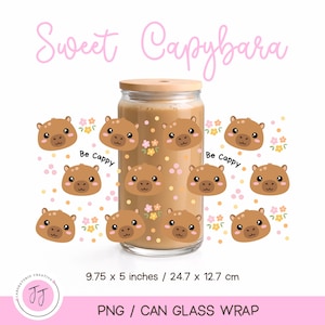 Può includere: Un bicchiere trasparente a forma di lattina con coperchio in legno, decorato con facce di capibara, fiori e la scritta "Sweet Capybara" e "Be Cappy". Il bicchiere misura 24,7 x 12,7 cm.