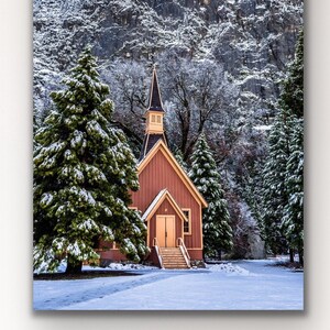 Könnte beinhalten: Gerahmter Leinwanddruck einer schneebedeckten Landschaft mit einer kleinen, roten Kirche mit Turm. Die Kirche ist von schneebedeckten Nadelbäumen und einem Berg umgeben. Der klare blaue Himmel rundet die Winterlandschaft ab.