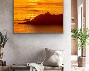 May include: A photograph of a lighthouse silhouetted against a fiery orange sunset over the ocean. The sky is filled with streaks of orange, pink, and yellow clouds. The lighthouse is a small, white structure with a red roof.