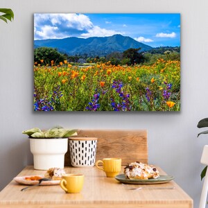 Puede incluir: Una fotograf&iacute;a de paisaje colorida que presenta un campo de flores silvestres amarillas y moradas en primer plano, con una cordillera en el fondo. El cielo es azul con nubes blancas.