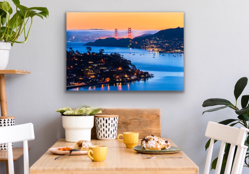 May include: A panoramic view of the Golden Gate Bridge at sunset, with the city lights twinkling in the distance. The bridge is a vibrant red against the orange and blue sky, with the water reflecting the colors.