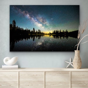 May include: A night sky filled with stars and the Milky Way galaxy reflected in a still lake. Silhouettes of trees line the shore.
