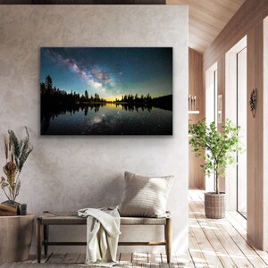 May include: A photograph of a starry night sky reflected in a still lake. The Milky Way is visible in the sky, and the trees on the shore are silhouetted against the light.