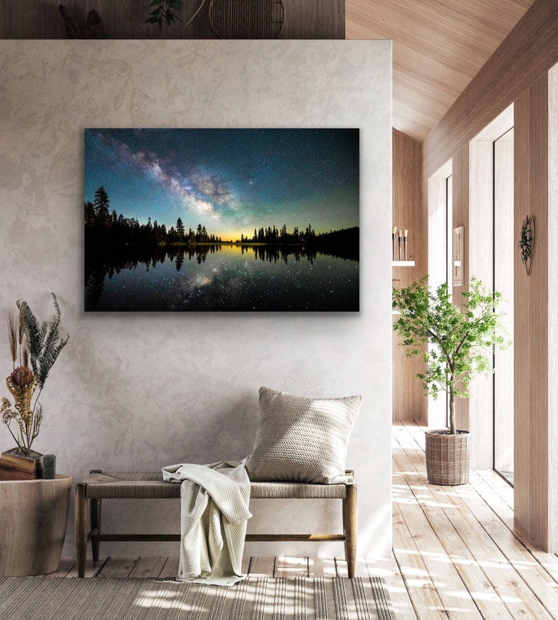May include: A photograph of a starry night sky reflected in a still lake. The Milky Way is visible in the sky, and the trees on the shore are silhouetted against the light.