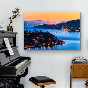 May include: A panoramic view of the Golden Gate Bridge at sunset, with the city lights twinkling in the distance. The bridge is a vibrant red against the orange and blue sky, with the water reflecting the colors of the sunset.