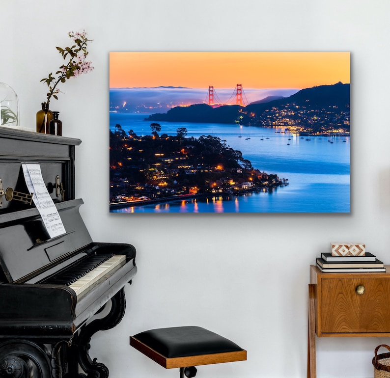 May include: A panoramic view of the Golden Gate Bridge at sunset, with the city lights twinkling in the distance. The bridge is a vibrant red against the orange and blue sky, with the water reflecting the colors of the sunset.