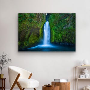 K&ouml;nnte beinhalten: Ein Foto eines Wasserfalls, der eine mit Moos bedeckte Felswand hinunterst&uuml;rzt. Das Wasser ist leuchtend blau und die umliegende Vegetation ist ein sattes Gr&uuml;n.