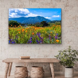 Puede incluir: Un vibrante campo de flores silvestres amarillas y naranjas con un fondo de cielo azul y colinas.