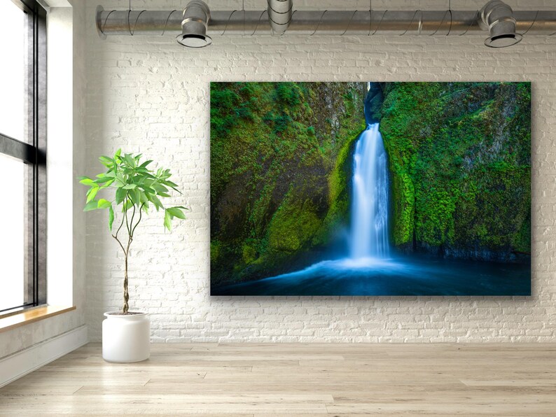 K&ouml;nnte beinhalten: Ein Foto eines Wasserfalls, der einen mit Moos bewachsenen Felsen hinunterst&uuml;rzt. Das Wasser ist leuchtend blau und die umliegende Vegetation ist ein sattes Gr&uuml;n.