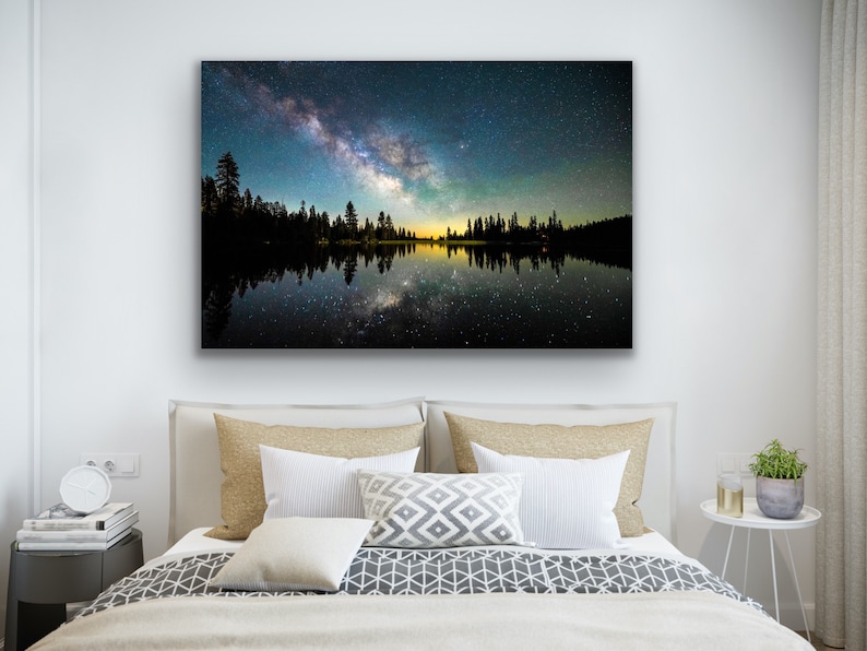 May include: A photograph of a starry night sky reflected in a still lake. The Milky Way is visible in the sky, and the trees on the shore are silhouetted against the light.