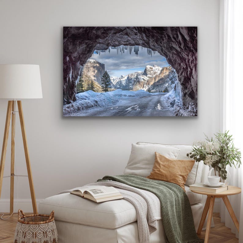 K&ouml;nnte beinhalten: Ein Leinwanddruck einer Winterlandschaft. Das Bild zeigt eine Stra&szlig;e, die sich durch ein verschneites Tal schl&auml;ngelt, eingerahmt von einem nat&uuml;rlichen Felsbogen mit Eiszapfen. Schneebedeckte Berge und ein bew&ouml;lkter Himmel vervollst&auml;ndigen die malerische Szene.