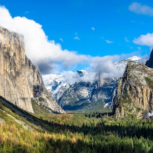 Könnte beinhalten: Ein Panoramablick auf ein Tal im Yosemite-Nationalpark, Kalifornien. Das Tal ist umgeben von hoch aufragenden Granitfelsen, von denen einige mit Schnee bedeckt sind. Ein Wasserfall stürzt an einer der Klippen herab. Der Talboden ist von einem dichten Kiefernwald bedeckt.