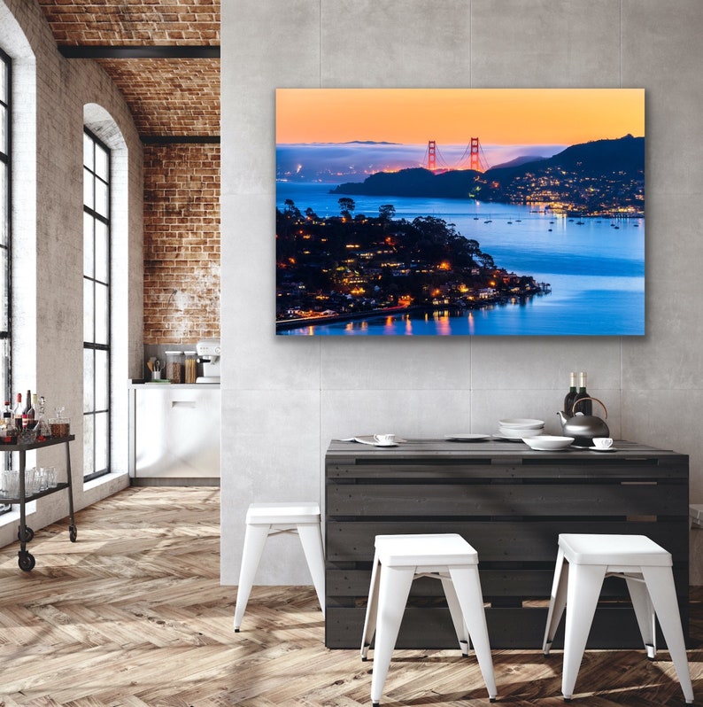 May include: A panoramic view of the Golden Gate Bridge in San Francisco, California at dusk. The bridge is lit up in orange and the water is a deep blue. The city lights are visible in the distance.