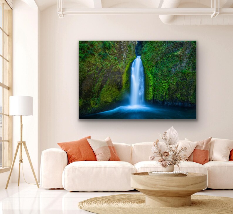 K&ouml;nnte beinhalten: Ein Foto eines Wasserfalls, der eine mit Moos bedeckte Felswand hinunterst&uuml;rzt. Das Wasser ist leuchtend blau und die umliegende Vegetation ist ein sattes Gr&uuml;n.