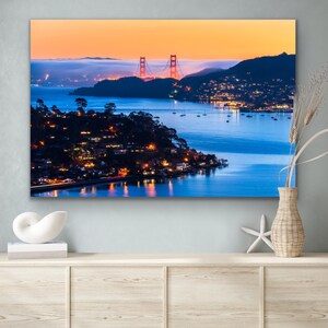 May include: A panoramic view of the Golden Gate Bridge at sunset, with the bridge illuminated in red and the surrounding cityscape glowing with lights. The water is calm and reflects the sky and the bridge.