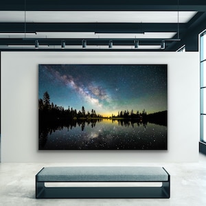 May include: A photograph of a starry night sky with the Milky Way galaxy reflected in a still lake. The lake is surrounded by a dark silhouette of trees.