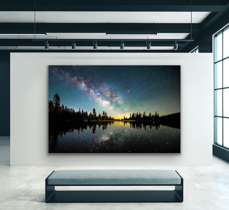 May include: A photograph of a starry night sky with the Milky Way galaxy reflected in a still lake. The lake is surrounded by a dark silhouette of trees.