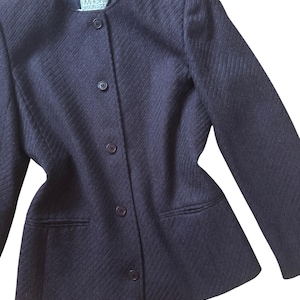 Puede incluir: Una blazer azul marino con un patrón de tejido diagonal texturizado. La blazer tiene cuello redondo, tres botones y dos bolsillos delanteros. La etiqueta dice "MAGNIN DESIGN STUDIO".