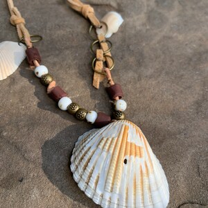 May include: A white seashell necklace with brown leather cord, white and brown beads, and gold-toned metal accents.