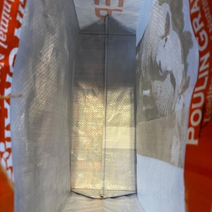 May include: Inside view of a large, open, white and gray woven bag. The bag has a rectangular shape with a folded bottom. The word "FEED" is visible in orange letters on the top edge. The bag is likely for animal feed.