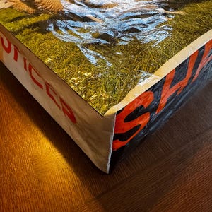 May include: A large, rectangular tote bag with a glossy, textured surface. The top of the bag features a pastoral scene of sheep grazing in a green field. The sides display the word "SALES" in red block letters against a black background.