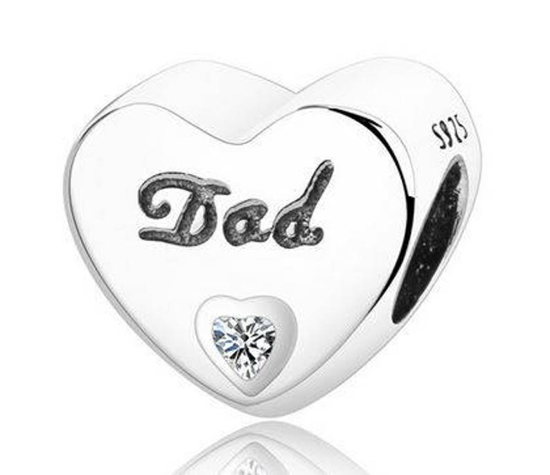 May include: A silver heart-shaped charm with the word "Dad" in a decorative font. A small heart-shaped gem is set at the bottom. The charm is marked with "S925".