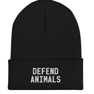May include: Black beanie with the words "DEFEND ANIMALS" embroidered in white. The beanie is a knit cap, suitable for cold weather. The text is centered on the front of the hat.
