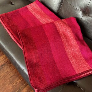 May include: Two red and pink striped blankets are folded on a dark brown leather couch. The blankets have a soft, fuzzy texture and are in shades of red, pink, and fuchsia. The couch has a tufted design.