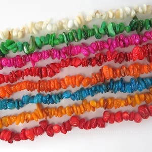 May include: A collection of colorful, chip-style beads in various shades, including white, green, pink, red, orange, and blue. The beads are arranged in parallel rows, showcasing their vibrant hues and irregular shapes. The image is set against a white background.