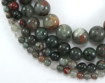 May include: A strand of round, green, brown, and white gemstone beads. The beads are various sizes and have a mottled, marbled appearance.