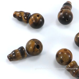 May include: A set of brown and gold tiger eye beads with a hole drilled through the center of each bead. Some of the beads are round and some are shaped like a small bottle.