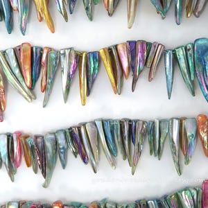 May include: Rows of iridescent, elongated beads in shades of blue, green, gold, and pink. The beads have a pointed, triangular shape and are strung together. The background is white. The Etsy shop URL is visible in the bottom right corner.