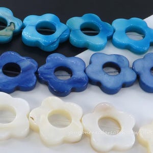 May include: Rows of flower-shaped beads in shades of blue and white. The beads have a hole in the center, and the colors range from light blue to deep navy and creamy white. The beads are likely for jewelry making.