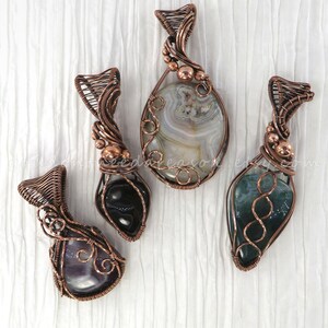 May include: Four handcrafted gemstone pendants with copper wire wrapping. The pendants feature various polished stones in shades of gray, green, black, and purple. Each pendant has a unique wire design, with intricate details and textures.