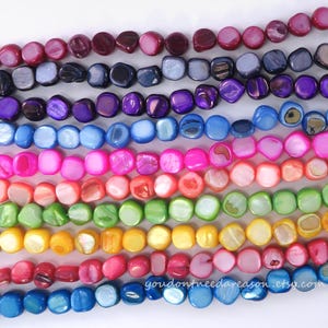 May include: Rows of colorful, polished shell beads in various shades, including red, purple, blue, green, and yellow. The beads are arranged in horizontal lines, showcasing their iridescent surfaces. The Etsy shop URL is visible at the bottom.