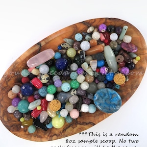 May include: A wooden bowl filled with a variety of colorful beads. The beads are in various shapes, sizes, and colors, including blue, green, pink, and purple. The text on the image says "This is a random 8oz sample scoop."