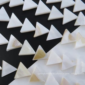 May include: Close-up of white triangular shell beads arranged in rows against a black and white background. Some beads have subtle beige and gold tones. The Etsy shop URL "youdontneedareason.etsy.com" is visible.