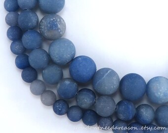 May include: A strand of blue agate beads in various shades of blue, ranging from light to dark. The beads are round and have a matte finish. The beads are arranged in a semi-circle shape.
