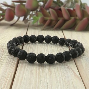 May include: A black lava rock beaded bracelet. The bracelet is made of round, black beads with a rough, textured surface.