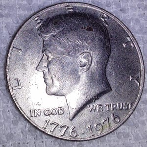 May include: A silver coin featuring a profile of a man, with the inscriptions "IN GOD WE TRUST" and "LIBERTY". The coin is dated 1776-1976.