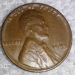 May include: A bronze-coloured 1955 Lincoln penny. The obverse shows a profile of Abraham Lincoln, the word "LIBERTY", and the inscription "IN GOD WE TRUST". The year "1955" is also visible.