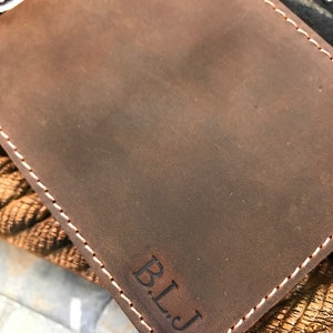 May include: A brown leather wallet with a stitched edge and the initials "B.L.J." embossed on the front.